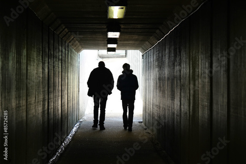 Two persons walk to the light in the end of the tunnel.