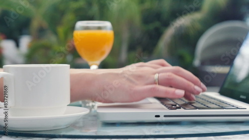 Close up of woman's hands typing on a laptop computer outdoors.
