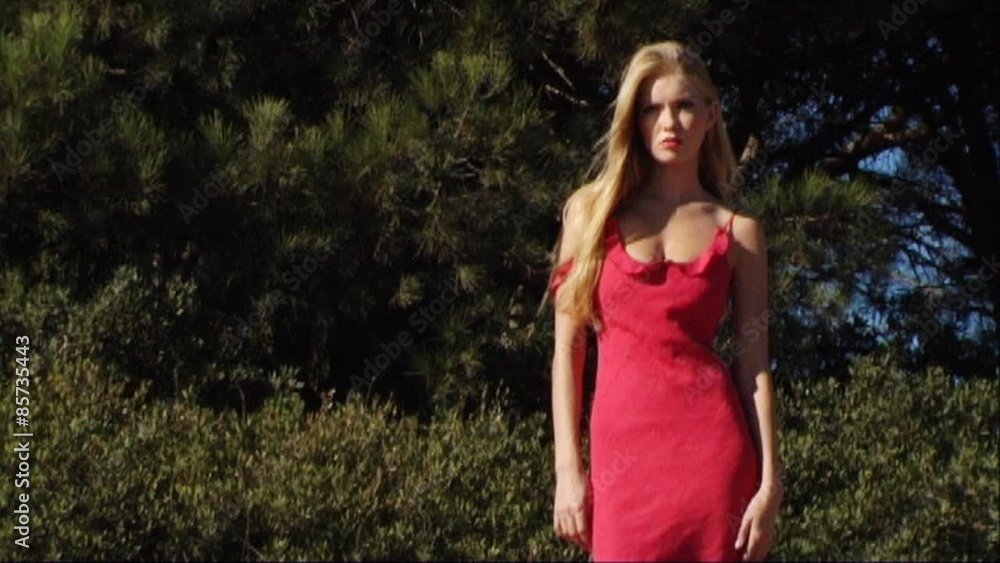 woman in red dress in front of tree with her hair blowing in breeze woman in red dress in front of tree with her hair blowing in breeze