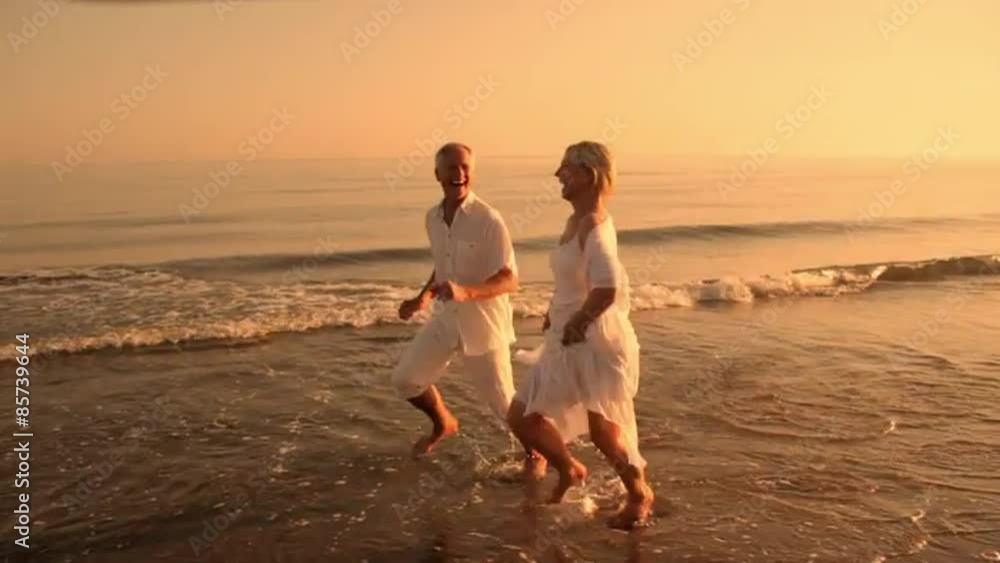 pan shot of senior couple running on beach in sunset pan shot of senior couple running on beach in sunset