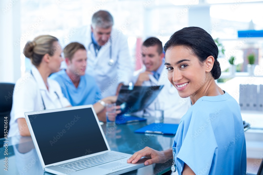Beautiful smiling doctor typing on keyboard with her team behind