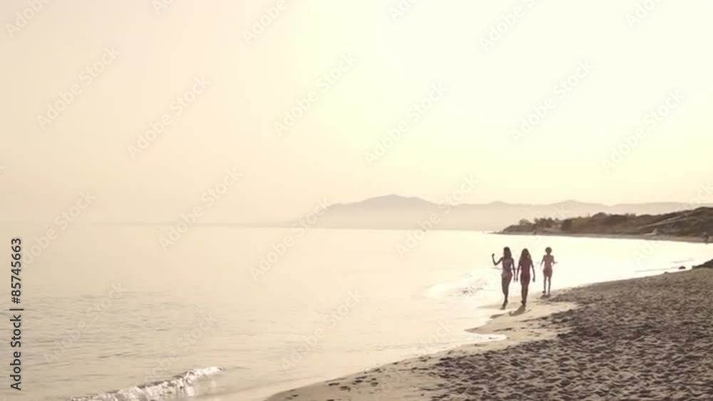 Three children running and walking to camera on beach.