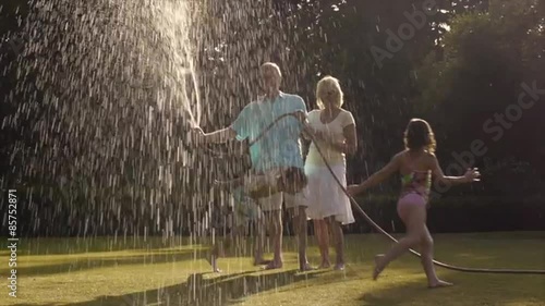 Grandchildren and grandparents in garden playing with water spray.