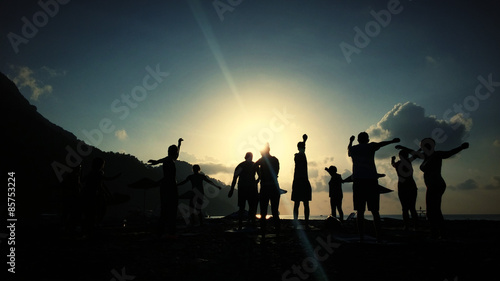 Silhouette of people doing Yoga at sea coast sunrise time