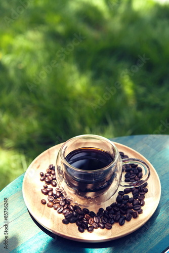 Hot Americano on wooden table green grass background