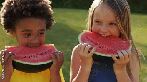 Two children eating water melon in park.