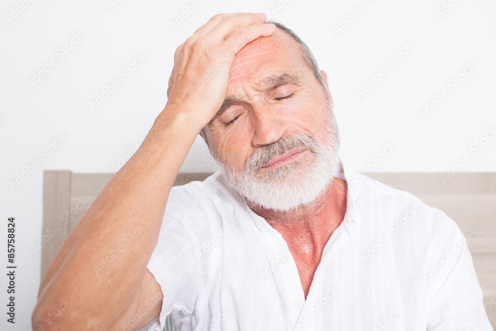 Obraz premium Elderly man sitting on bed suffering from headache