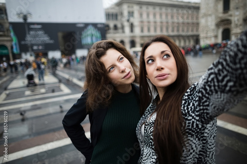 Two girls taking pictures of themselves on the town square © ilya_oreshkov