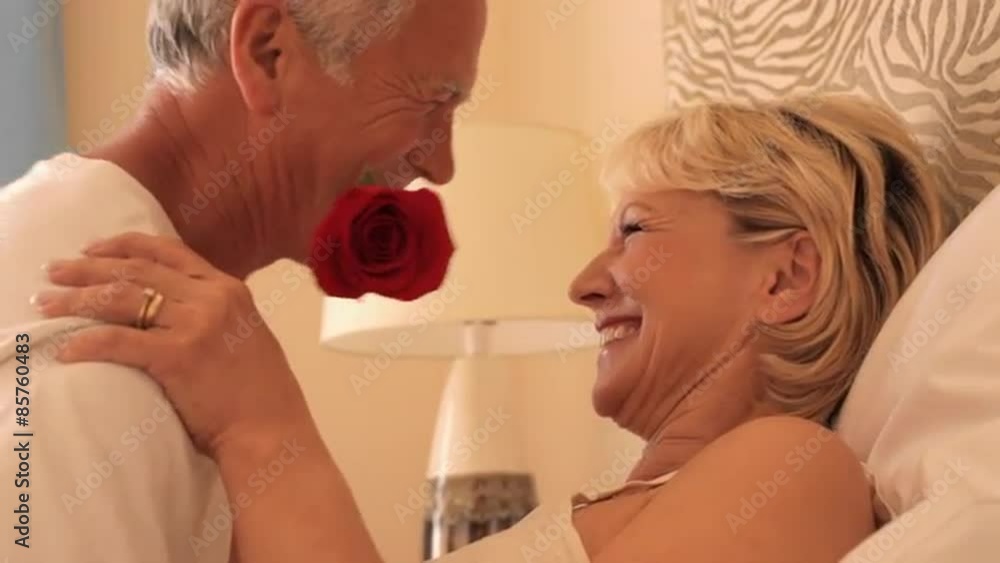 senior couple sitting in bed man with red rose in teeth senior couple sitting in bed man with red rose in teeth