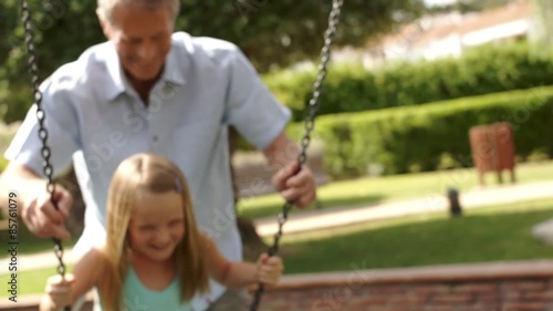 Slow motion of grandfather pushing granddaughter on swing in park.