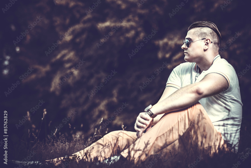 Brutal man in sunglasses sitting on the ground outdoor Brutal man in sunglasses sitting on the ground outdoor