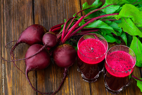 Glass of fresh beetroot juice with bets on wooden table