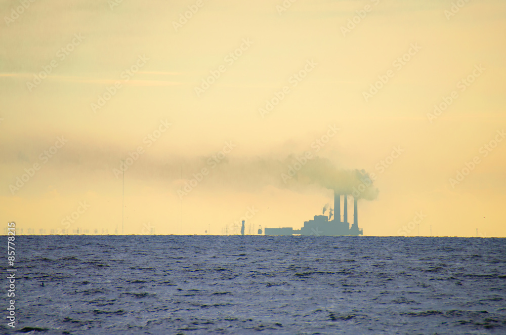 Heavily polluted smoke billowing from a power plant on the edge of a large bay of water. Heavily polluted smoke billowing from a power plant on the edge of a large bay of water.