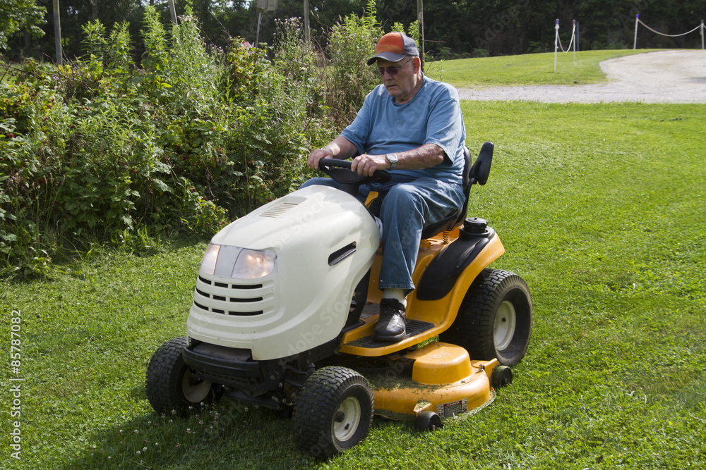 Fototapeta premium Older Male Mowing Grass With His Riding Mower
