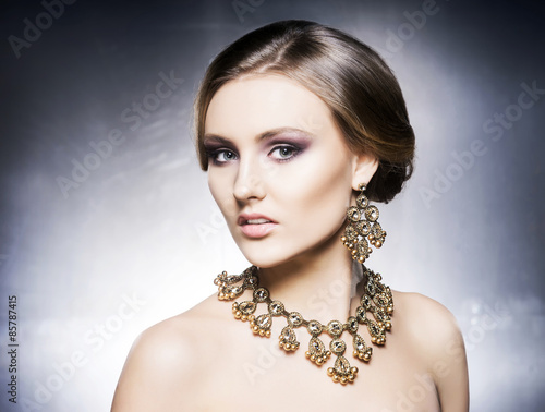 Young, beautiful and rich woman in jewels. Metal background