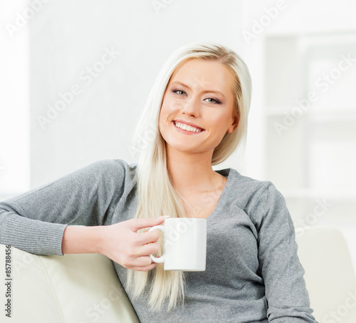 Young and happy woman resting on sofa at home and drinking coffee