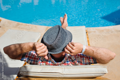Fototapeta man in a hat lying on a lounger by the pool