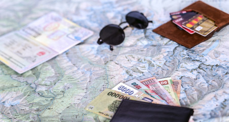 Higher contrast composition on travel topic. 
Unfolded detailed topographic map exotic Asian cash notes credit cards sunglasses passport entry stamps many