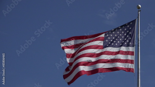 Beautiful jumbo American flag waving on top of a flag pole with a blue sky.