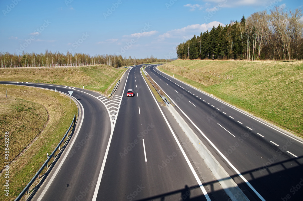 Asphalt expressway with slip road in the landscape. Traveling alone red car. Asphalt expressway with slip road in the landscape. Traveling alone red car.