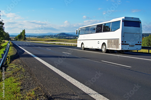 White Bus driving on an empty road in a rural landscape
