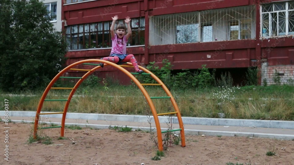 Little girl sits on semicircular ladder and waves hand at playground
Little girl sits on semicircular ladder and waves hand at playground