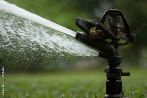 A sprinkler is watering grass field in a park. This device sprays the water up to 30 meters away.