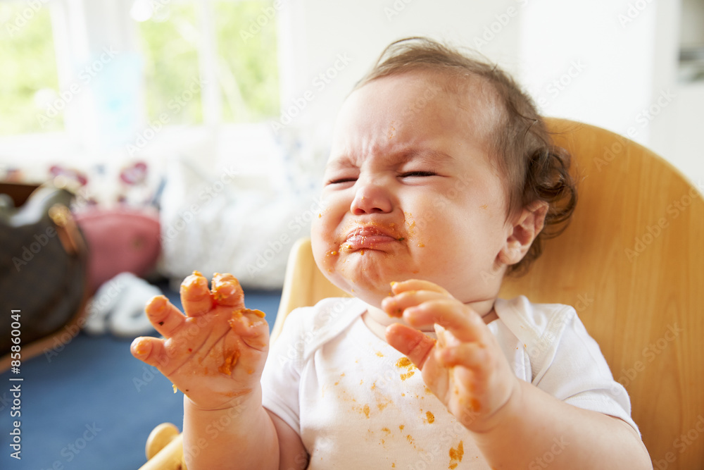 Wall Mural Unhappy Baby In High Chair At Meal Time