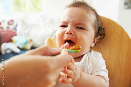 Photos Unhappy Baby Being Fed In High Chair At Meal Time
