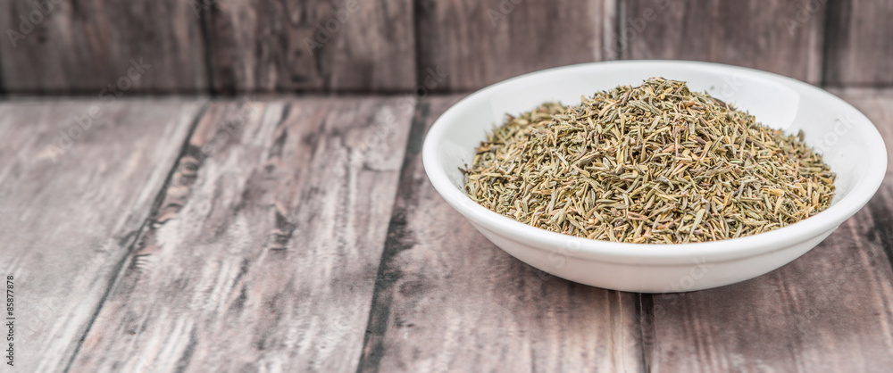 Dried thyme herbs in white bowl over weathered wooden background Dried thyme herbs in white bowl over weathered wooden background