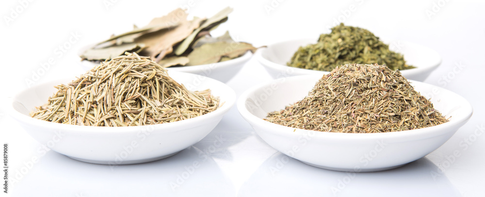 Rosemary, parsley, bay leaves and thyme in white bowl over white background