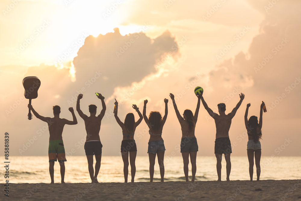Group of friends raising hands on the beach at sunset