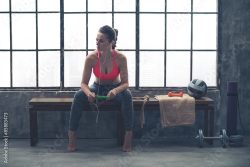 Woman sitting on bench in loft gym listening to music on device