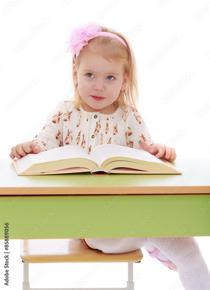Happy joyful blonde girl is reading a thick book sitting on the Happy joyful blonde girl is reading a thick book sitting on the