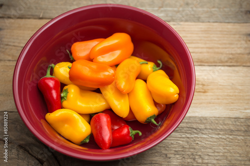 Bell peppers in a red bowl on weathered wood background.