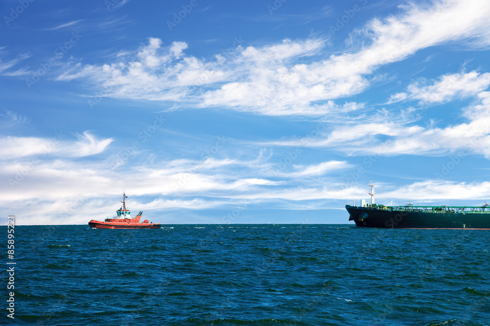 Obraz premium Tug boat towing a tanker ship at sea.