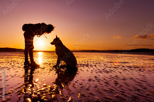 Hipster girl playing with dog at a beach during sunset  silhouettes with vibrant colors