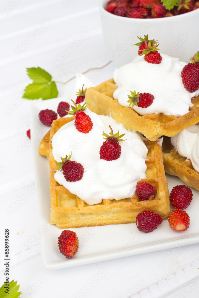 waffles with wild strawberries and whipped cream on white table waffles with wild strawberries and whipped cream on white table