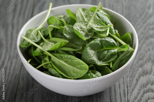 fresh spinach leaves in white bowl on wood table
