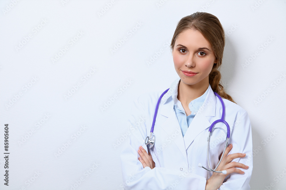 Friendly smiling young female doctor, standing near wall Friendly smiling young female doctor, standing near wall