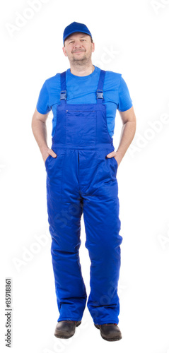 Man in blue overalls with hands in pockets.