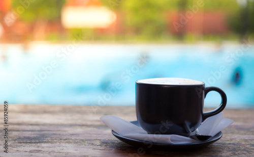 Cup of coffee on wooden deck near Swimming pool
