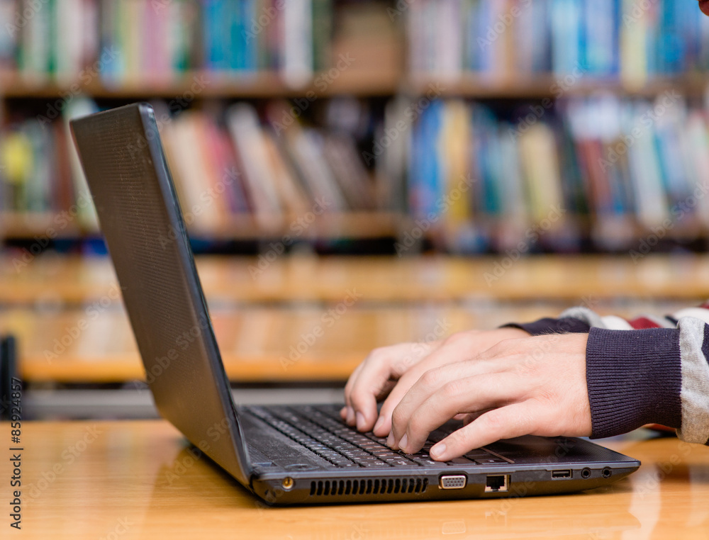 Hands typing on notebook in library Hands typing on notebook in library
