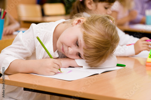 tired schoolgirl writes in a notebook during lesson