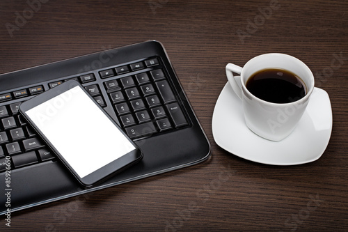 Top view on dark wooden office desk with computer keyboard, mobile with blank screen and cup of cofee.