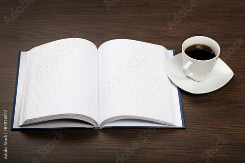 Top view on dark wooden office desk with opened book and cup of coffee.