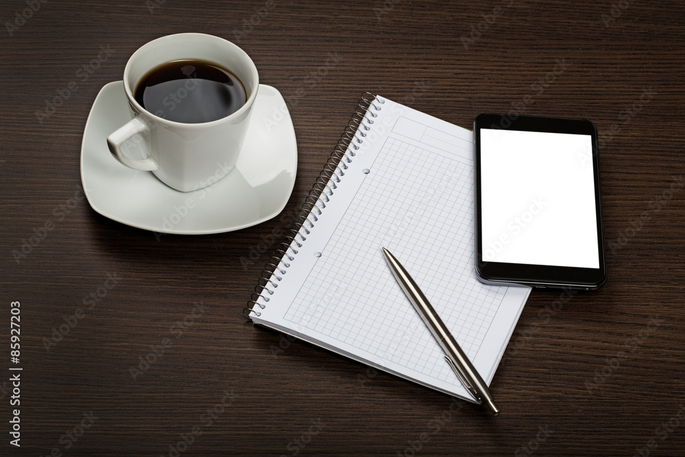 Top view on dark wooden office desk with notepad, pen, modern mobile with blank screen and cup of cofee. Top view on dark wooden office desk with notepad, pen, modern mobile with blank screen and cup of cofee.
