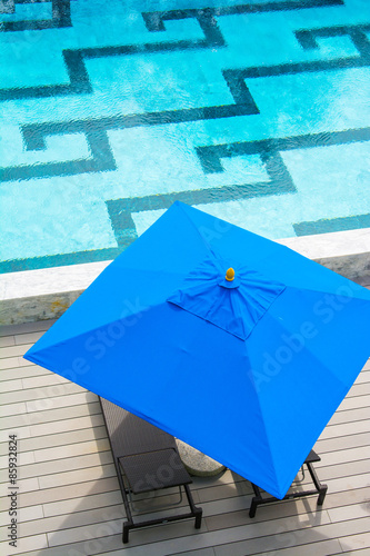 beach chair and blue umbrella by the pool