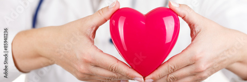 Female medicine doctor's hands holding red toy heart