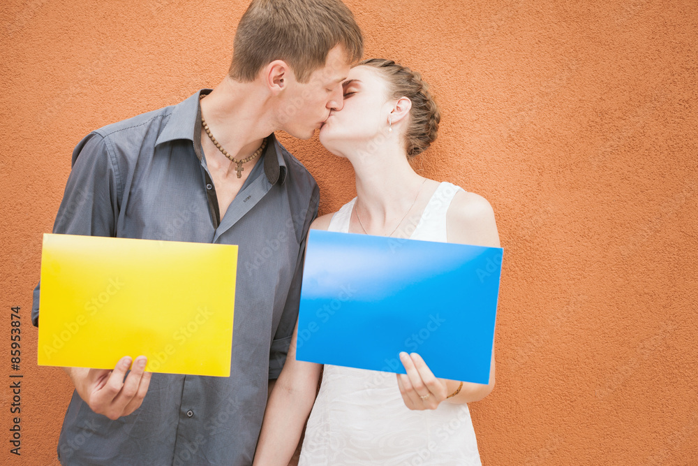 Funny young couple kissing and holding yellow and blue frame at red  background. Image ready for